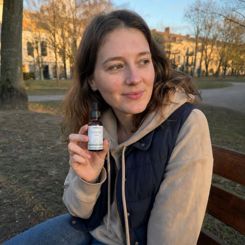 Woman holding a bottle of Lucerne CBD oil outdoors in a park
